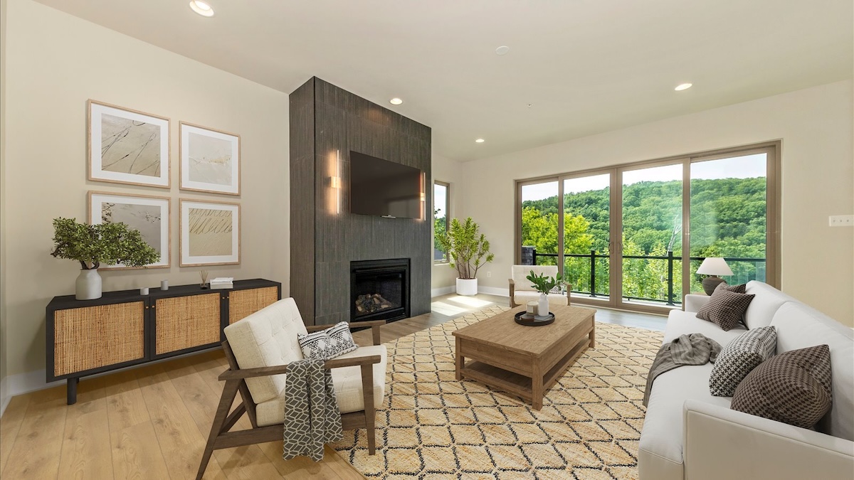 modern living room with fireplace, mounted TV, and wall of windows overlooking wooded views in a custom built home