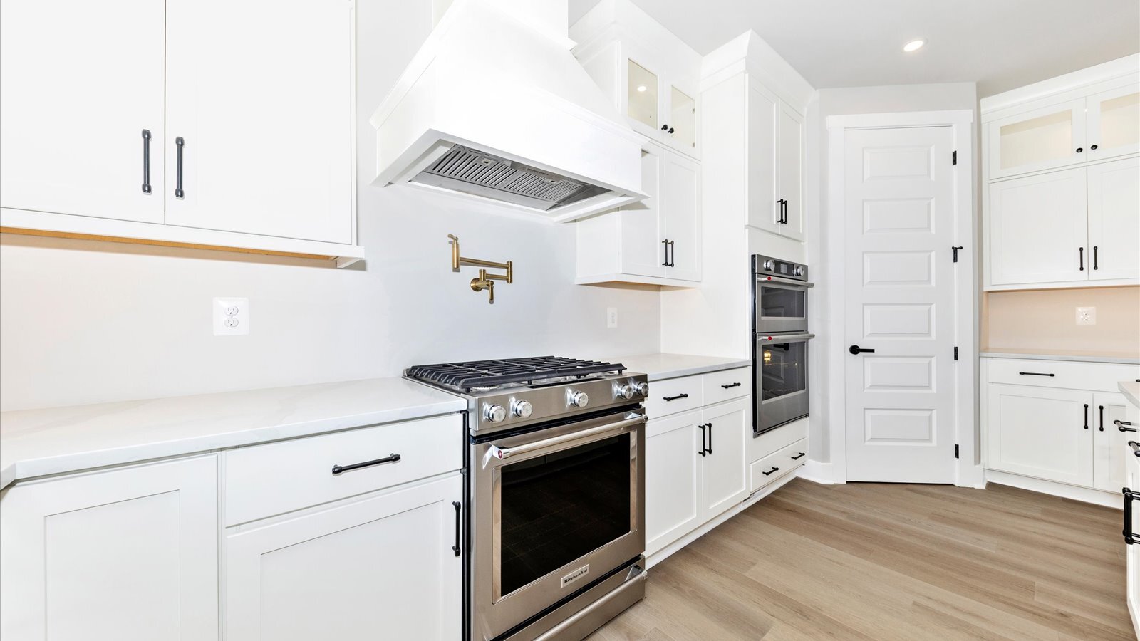 modern white kitchen with gold fixtures, gas range, and built-in double wall oven in a custom built home